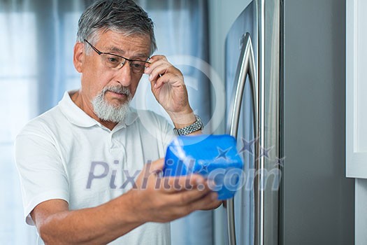 Is this still fine? Senior man in his kitchen by the fridge, looking at the expiry date of a product she took from her fridge - Is this still fine? Senior man in his kitchen by the fridge, looking at the expiry date of a product she took from her fridge -