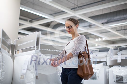 Pretty, young woman choosing the right pillow for her bed in a modern home furnishings store (color toned image; shallow DOF) Pretty, young woman choosing the right pillow for her bed in a modern home furnishings store (color toned image; shallow DOF)