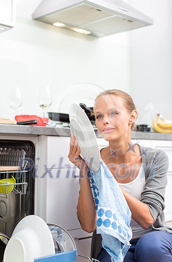 Young woman washing dishes in her modern kitchen, using a dishwasher, putting the dishes in their place Young woman washing dishes in her modern kitchen, using a dishwasher, putting the dishes in their place