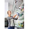 Young woman washing dishes in her modern kitchen, using a dishwasher, putting the dishes in their place