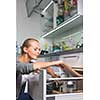 Young woman washing dishes in her modern kitchen, using a dishwasher, putting the dishes in their place