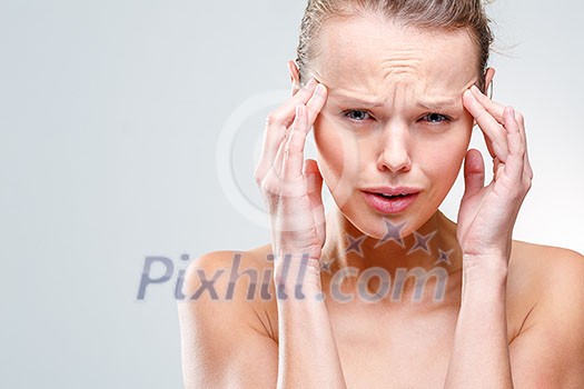 Beautiful woman suffering from acute headache over grey clean background, praying with her eyes for the pain to stop (shallow DOF; color toned image)