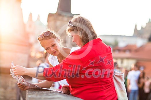 Mother and daughter traveling - two female tourists studying a map, discovering a new city Mother and daughter traveling - two female tourists studying a map, discovering a new city