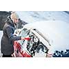 Young woman cleaning her car from snow and frost on a winter morning, she is freezing and needs to get to work