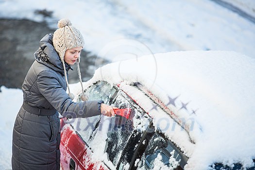Young woman cleaning her car from snow and frost on a winter morning, she is freezing and needs to get to work Young woman cleaning her car from snow and frost on a winter morning, she is freezing and needs to get to work