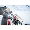 Young woman cleaning her car from snow and frost on a winter morning, she is freezing and needs to get to work