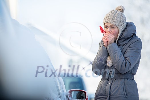 Young woman cleaning her car from snow and frost on a winter morning, she is freezing and needs to get to work Young woman cleaning her car from snow and frost on a winter morning, she is freezing and needs to get to work