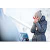 Young woman cleaning her car from snow and frost on a winter morning, she is freezing and needs to get to work