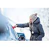 Young woman cleaning her car from snow and frost on a winter morning, she is freezing and needs to get to work