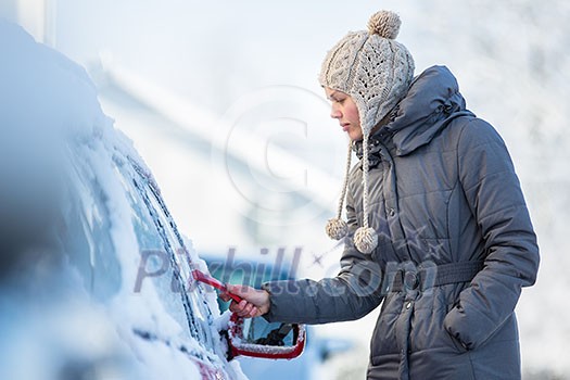 Young woman cleaning her car from snow and frost on a winter morning, she is freezing and needs to get to work Young woman cleaning her car from snow and frost on a winter morning, she is freezing and needs to get to work