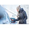 Young woman cleaning her car from snow and frost on a winter morning, she is freezing and needs to get to work