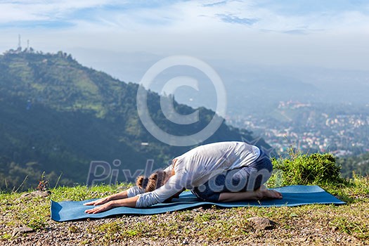 Sporty fit woman practices yoga asana Balasana - child pose outdoors in mountains Sporty fit woman practices yoga asana Balasana - child pose outdoors in mountains