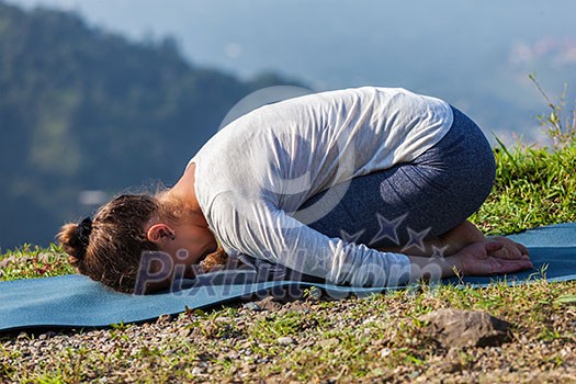 Sporty fit woman practices yoga asana Balasana - child pose outdoors in mountains Sporty fit woman practices yoga asana Balasana - child pose outdoors in mountains