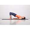 Beautiful sporty fit yogini woman practices yoga asana setu bandhasana - bridge pose beginner variation in studio