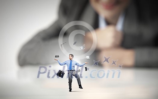 Businesswoman looking at miniature of man juggling with items Businesswoman looking at miniature of man juggling with items