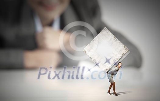 Businesswoman looking at miniature of woman carrying white cube on back Businesswoman looking at miniature of woman carrying white cube on back