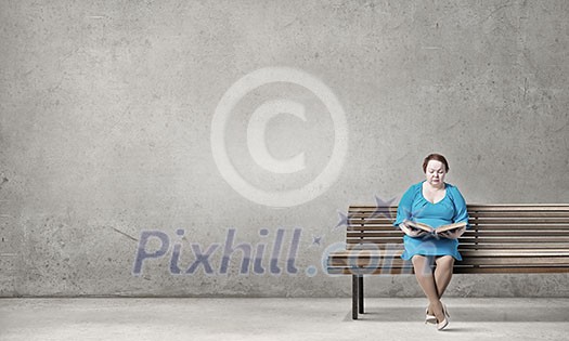 Plus size woman with book in hands sitting on bench Plus size woman with book in hands sitting on bench