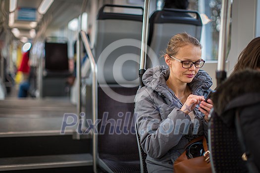 Pretty, young woman on a streetcar/tramway, during her commute to work. Using her smartphone. (color toned image; shallow DOF) Pretty, young woman on a streetcar/tramway, during her commute to work. Using her smartphone. (color toned image; shallow DOF)
