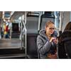 Pretty, young woman on a streetcar/tramway, during her commute to work. Using her smartphone. (color toned image; shallow DOF)