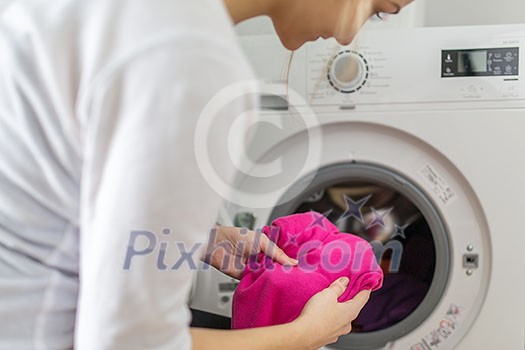 Housework: young woman doing laundry - putting colorful garments into the washing machine (shallow DOF; color toned image) Housework: young woman doing laundry - putting colorful garments into the washing machine (shallow DOF; color toned image)