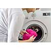 Housework: young woman doing laundry - putting colorful garments into the washing machine (shallow DOF; color toned image)