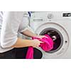 Housework: young woman doing laundry - putting colorful garments into the washing machine (shallow DOF; color toned image)