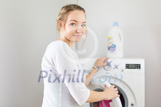 Housework: young woman doing laundry - putting colorful garments into the washing machine (shallow DOF; color toned image) Housework: young woman doing laundry - putting colorful garments into the washing machine (shallow DOF; color toned image)