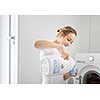 Housework: young woman doing laundry - putting colorful garments into the washing machine (shallow DOF; color toned image)