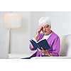 Portrait of a senior woman at home - Looking happy, looking at the camera, smiling while sitting on the sofa in her living room and reading a good book