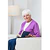 Portrait of a senior woman at home - Looking happy, looking at the camera, smiling while sitting on the sofa in her living room and reading a good book
