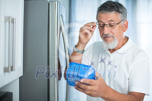 Is this still fine? Senior man in his kitchen by the fridge, looking at the expiry date of a product she took from her fridge - Is this still fine? Senior man in his kitchen by the fridge, looking at the expiry date of a product she took from her fridge -