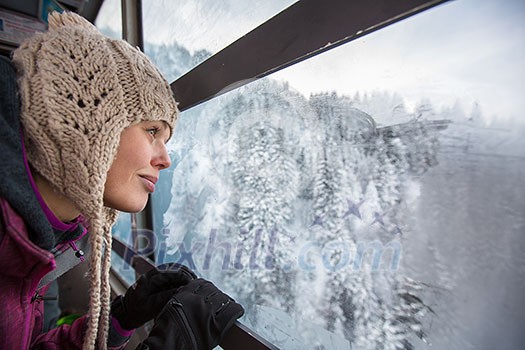 Pretty, young woman admiring splendid winter scenery from a cablecar cabin in high mountains (shallow DOF; color toned image) Pretty, young woman admiring splendid winter scenery from a cablecar cabin in high mountains (shallow DOF; color toned image)