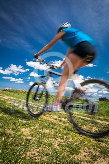 Pretty, young female biker outdoors on her mountain bike (motion blurred image)