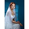 Beautiful bride on a blue background. Wedding dress, veil, red hair.