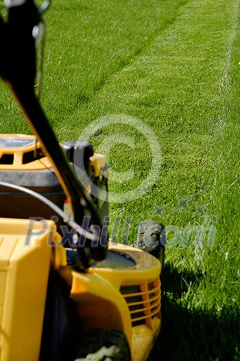 Yellow lawn mower on the green grass. Caring for a garden. Shallow depth of field. Focus on grass. Yellow lawn mower on the green grass. Caring for a garden. Shallow depth of field. Focus on grass.