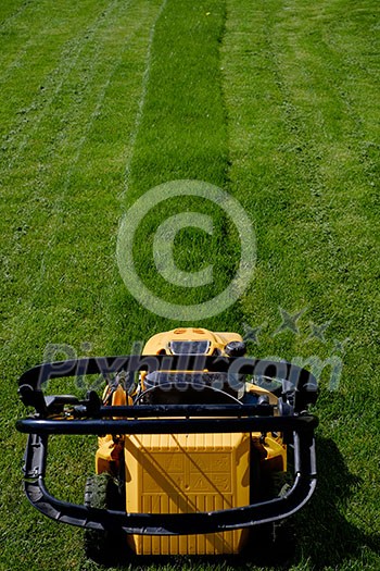 Yellow lawn mower on the green grass. Caring for a garden. Shallow depth of field. Yellow lawn mower on the green grass. Caring for a garden. Shallow depth of field.
