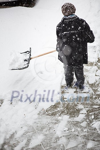 Man shoveling snow from the sidewalk in front of his house after a heavy snowfall in a city Man shoveling snow from the sidewalk in front of his house after a heavy snowfall in a city