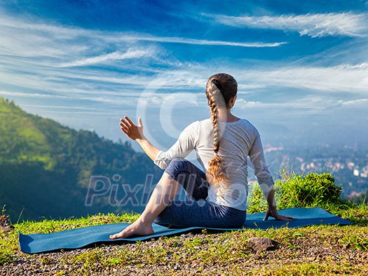 Sporty fit woman practices yoga asana Parivrtta Marichyasana - seated spinal twist outdoors in mountains in the morning Sporty fit woman practices yoga asana Parivrtta Marichyasana - seated spinal twist outdoors in mountains in the morning