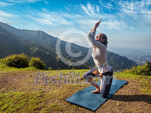 Young woman doing Ashtanga Vinyasa yoga advanced difficult asana Vatayanasana (Horse pose) outdoors in Himalayas mountains. Himachal Pradesh, India Young woman doing Ashtanga Vinyasa yoga advanced difficult asana Vatayanasana (Horse pose) outdoors in Himalayas mountains. Himachal Pradesh, India