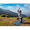 Young woman doing Ashtanga Vinyasa yoga advanced difficult asana Vatayanasana (Horse pose) outdoors in Himalayas mountains. Himachal Pradesh, India