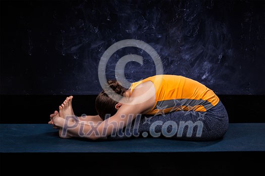 Sporty fit woman practices Ashtanga Vinyasa yoga back bending asana Paschimottanasana - seated forward bend Sporty fit woman practices Ashtanga Vinyasa yoga back bending asana Paschimottanasana - seated forward bend