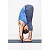 Sporty fit woman practices yoga asana Padahastasana - standing forward bend with hand under feet