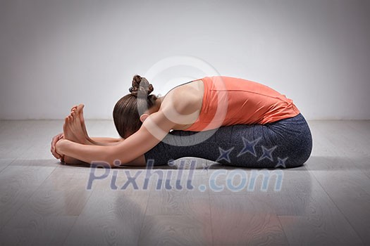 Sporty fit woman practices Ashtanga Vinyasa yoga back bending asana Paschimottanasana - seated forward bend Sporty fit woman practices Ashtanga Vinyasa yoga back bending asana Paschimottanasana - seated forward bend