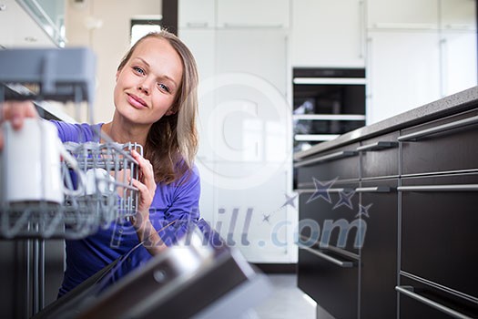 Pretty, young woman in her modern and well equiped kitchen putting cups into the dishwasher - an appliance that helps her keep the home tidy Pretty, young woman in her modern and well equiped kitchen putting cups into the dishwasher - an appliance that helps her keep the home tidy