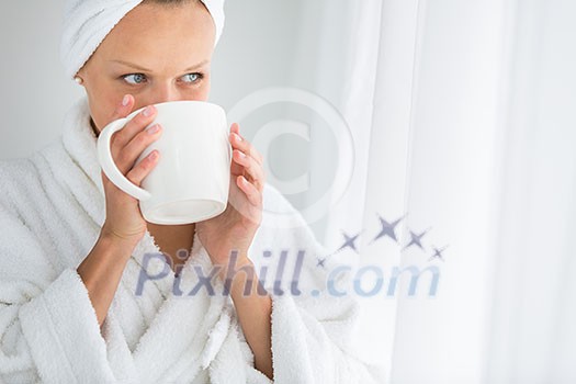Gorgeous young woman wearing a bathrobe and enjoying a mug hot tea, savouring every sip (shallow DOF; color toned image)