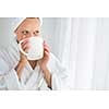 Gorgeous young woman wearing a bathrobe and enjoying a mug hot tea, savouring every sip (shallow DOF; color toned image)