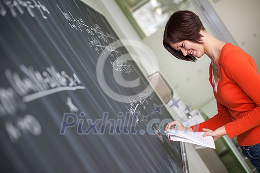 Pretty young college student/young teacher writing on the chalkboard/blackboard during a math class (color toned image) Pretty young college student/young teacher writing on the chalkboard/blackboard during a math class (color toned image)