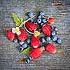 Fresh small wild strawberries and blueberries on old blue wooden background square format