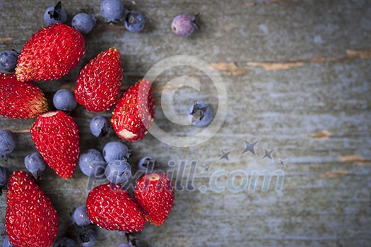 Fresh small wild strawberries and blueberries on old blue wooden background with copy space