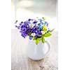 Bouquet of wild flowers in white vase on rustic wooden table near window, natural light